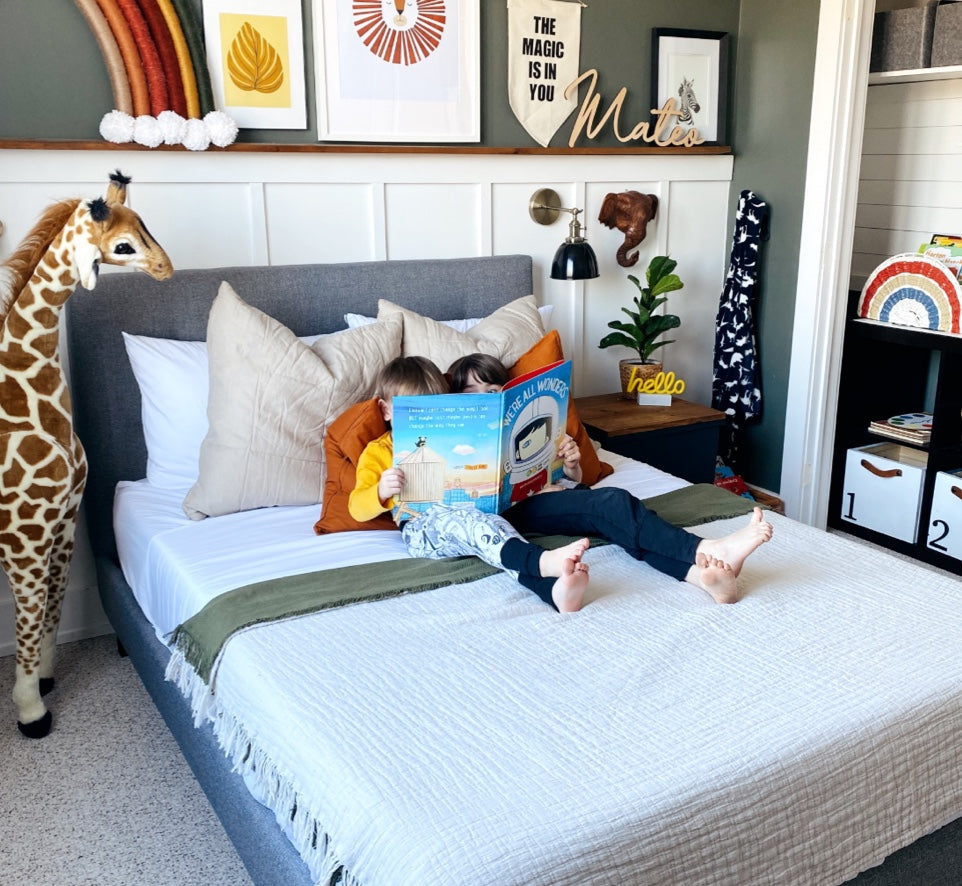 Two siblings snuggle together reading ‘We are the Monsters’ on their new Endy Upholstered Bed.